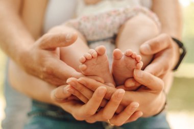İki el, erkek ve dişi tarafından tutulan çocuk bacaklarının yakın çekimi. Çocuk koruma. Bebek bakımı. Çocukların sağlığı için. Sevgi ve şefkat. Aile değerleri. Babalık ve annelik.