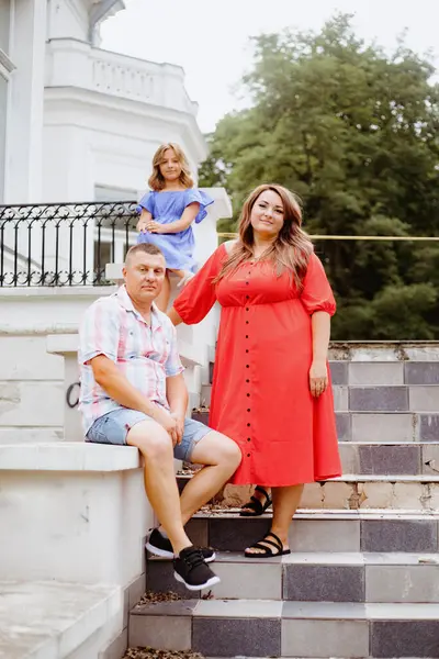 Vertical family portrait . Happy, beautiful family mom, dad, daughter pose against background of white building, old park. Harmonious family, mutual understanding, trust. Fatherhood ,motherhood.