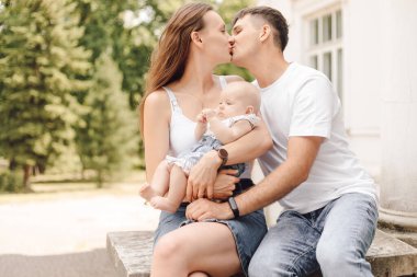Şefkat ve şefkat. Küçük çocuklu mutlu genç aile yaz gününün tadını çıkarıyor, ebeveynler öpüşüyor. Aile fotoğrafı. Çocukluğun korunması ve korunması. Genç bir aileye borç vermek. Aile değerleri.