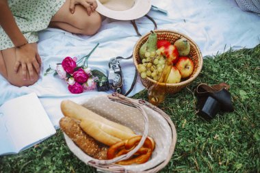 Tanınmayan bir kız piknik için beyaz masa örtüsünün üzerinde oturuyor. Meyveler, çiçekler, pastalar. Doğada harika bir yaz pikniği. Yaz tatili kavramı. Romantik bir randevu. Dinlenme zevki. 