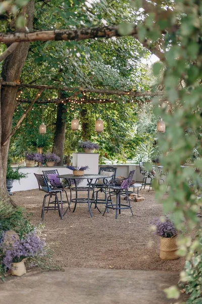 Ideal place to enjoy summer day in nature. Wrought-iron black tables and chairs on gravel area surrounded by tall trees are decorated with bouquets of lavender. Scents of sun and lavender.