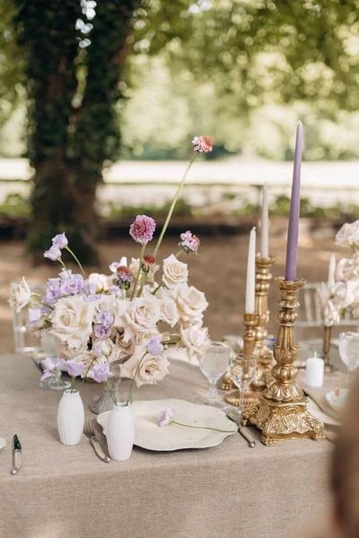 Design and serving of festive wedding table in natural colors with luxurious bouquets of roses, crystal, porcelain, vintage bronze candlesticks.Hotel, restaurant business. Wedding floristry design.