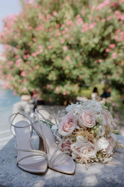 Wedding accessories. Open wedding shoes with rhinestones and delicate bouquet of bride onlarge stone in nature on beautiful summer day. Romantic mood. Wedding event. Organization of weddings.