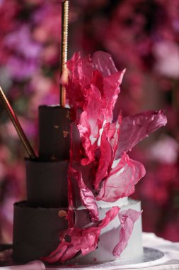 Beyaz ve çikolatalı üç katlı, egzotik çiçek yapraklarıyla süslenmiş düğün pastası gerçek bir şekerleme sanatı eseridir. Sipariş için kek yapıyorum. Şekerleme ürünleri. Tatlılar, pastalar. Şeker çubuğu.