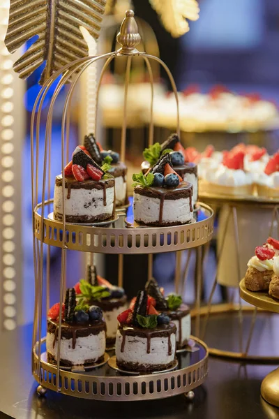 Cakes similar to small cakes , decorated with fresh berries stand on two - level round at wedding event, party, holiday. Enjoying taste. Making cakes to order. Desserts and pastries.