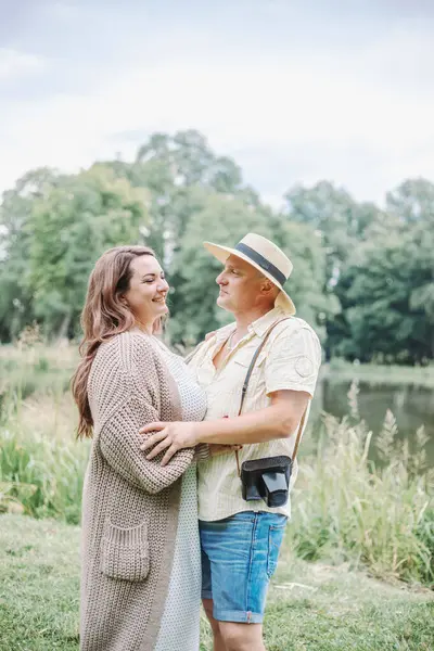 Beautiful smiling brown - haired woman inlong knitted cozy cardigan hugs her husband on summer day in nature. Harmonious loving happy family. Right relationship. Positive emotions. Happy together.