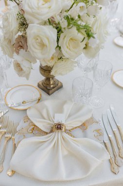 Kutlamaların organizasyonu. Klasik tabaklar, gümüş eşyalar, klasik yüzüklü peçete, kristal ve buket narin güllerle düğün masasının dikey görüntüsü.. 
