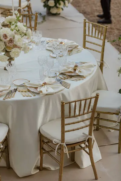 Stylish luxurious wedding table in white tones, with classic bouquets, silverware and white napkins. Decoration of festive events. Wedding in white tones. Work of florists. Hotel, restaurant business.