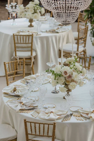Decoration of festive events.Stylish luxurious wedding table in white tones, with classic bouquets, silverware white napkins. Wedding in white tones. Work of florists. Hotel restaurant business.
