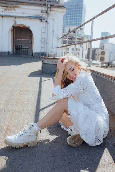 Olumlu duygular. Uzun, gevşek saçlı kadın, gözlerini kapatan, gülümseyen, şehir binasının çatısında oturan, gökdelenlerin arkaplanına karşı yaz sabahı. Romantik ruh hali. 