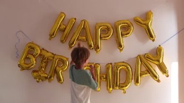 Mutlu çocuk 6-8 altın balonlardan yapılmış doğum günü duvarındaki yazıya bakar, elleriyle mektuplara dokunur. Doğum günü partisi hazırlanıyor. Sevgi ve ilgi. Tatil beklentisi. 4k görüntü