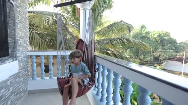 Αγόρι Λικνίζεται Κουνιστή Καρέκλα Μεγάλο Ανοιχτό Μπαλκόνι Στο Ξενοδοχείο Κοιτάζοντας — Αρχείο Βίντεο
