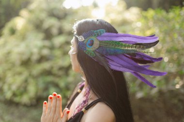 Tanımlanamayan bir kadın sırtı dönük, avuçları dua jesti ile kıvrılmış, kafasında Hint tarzı tüy süsü vardı. Meditasyon. Harmony, kendini arama. Gelenek ritüelleri. Özerklik.