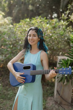 Çekici kadın, sanatçı, gitarist doğada gitar çalıyor, geleneksel Hint başlığı takmış, tüylü. Ruhsal miras. Etnik unsurlar. Harmony, kendini arama. Gelenekler ve ritüeller.