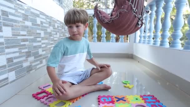 Uroczy Chłopiec Gołymi Stopami Siedzi Podłodze Balkonie Przed Wycieraczką Alfabetem — Wideo stockowe