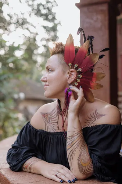 Adult beautiful woman with tattoos on her body and with beautiful feather decoration on her head enjoys tranquility of summer day. Tourism and travel. Confident women. Happiness and serenity.