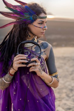 Canlı mor elbiseli bir kadın bir çift elektrikli mavi kulaklıkla aksesuar takıyor. Kıyafeti moda tasarımı ve sahne sanatları estetiğinin moda bir karışımı.