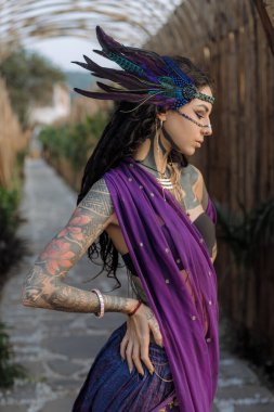 Menekşe elbiseli ve tüylü başlıklı bir kadın zarif bir şekilde kaldırımda duruyor ve resmi bir etkinlikte göz kamaştırıcı bir moda tasarımı sergiliyor.