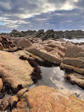 Kaya havuzları kumsalda alçak gelgitte, kara bulutlar gökyüzünde toplanıyor. Povoa de Varzim, Portekiz.
