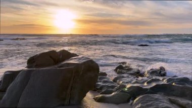 Gün batımında Portekiz 'de büyük kayaların üzerinde hafif okyanus dalgaları süzülüyor. Önde büyük bir kaya var. Güzel pastel gökyüzü.