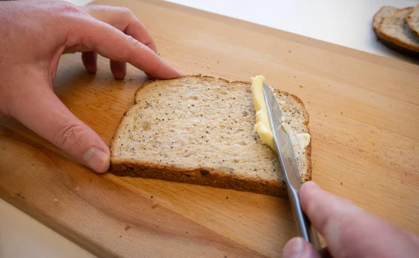 Dilimlenmiş kahverengi ekmeğe tereyağı sürüyorum..