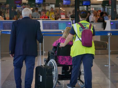 Operatör, havaalanında hareket etmek için tekerlekli sandalyede oturan bir bayana destek veriyor..
