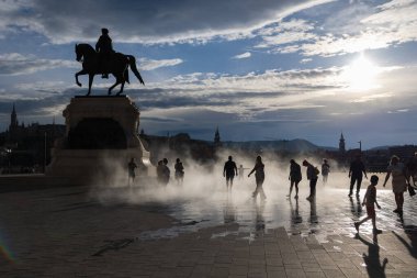 The Bronze Equestrian Statue of Count Gyula Andrssy backlighting in Kossuth Square near the building of Parliament and children playing with water vapor, Budapest, Hungary clipart