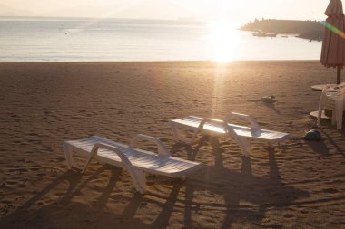 Plaj sandalyeleri gün doğumunda sahilde.