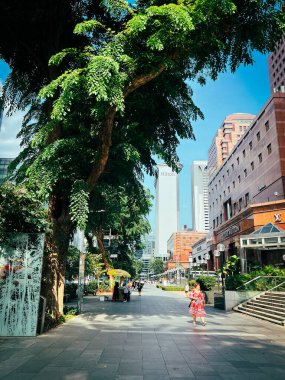 Sıcak, güneşli bir günde alışveriş yaptıktan sonra Orchard Yolu 'nda gezinen biri.