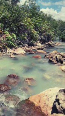 Tomohon, Güney Sulawesi dağlarındaki yeşilliklerle çevrili buharlaşan doğal kaplıcalara akan suyun sabitlenmiş doğa görüntüsü. Dikey Görünüm