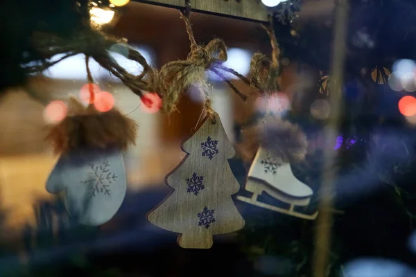 Wooden Christmas decorations stylized as a Christmas tree, mittens and skates, suspended by strings on the inscription bar, framed by fir branches. Selective focus with blurred background.