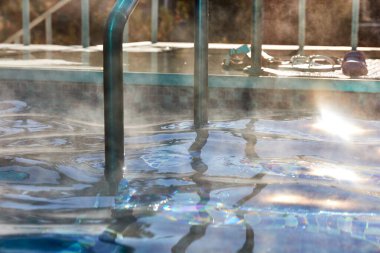 Mavi su ve mozaik kaplı zemini olan havuza inin. Suyun üstünde buhar. sıcak bahar havuzu