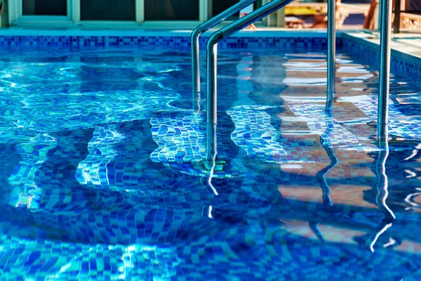 Mavi su ve mozaik kaplı zemini olan havuza inin.