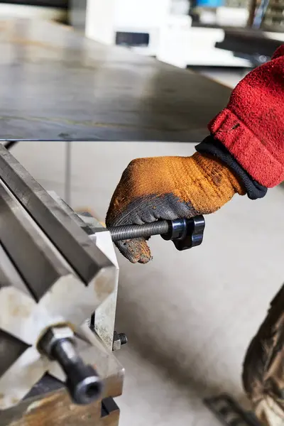 a worker\'s gloved hand on the adjusting screw of a bending machine