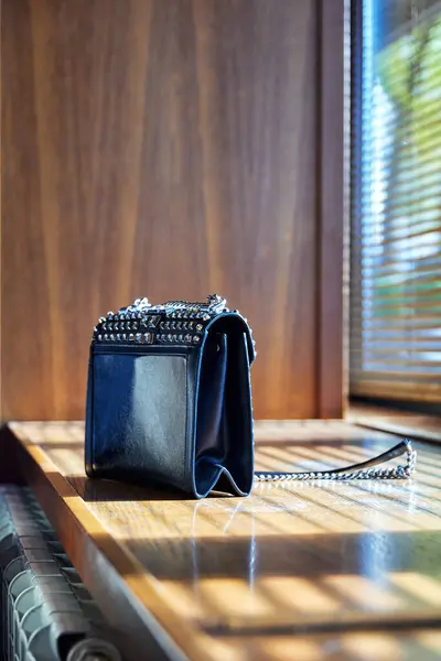 a clutch or a womans handbag on the windowsill with shadows from the blinds