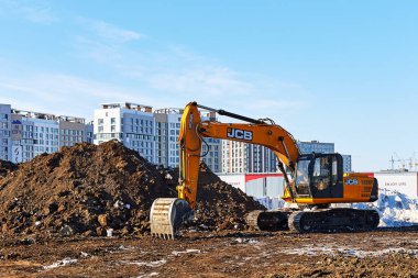 İnşaat alanındaki JCB kazıcısı, konut binalarının arka planına karşı. Astana, Kazakistan