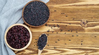 Rice berry in a bowl and spoon on a wooden table.