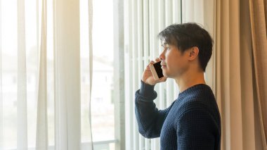 Asyalı bir adam odada akıllı telefon kullanıyor..