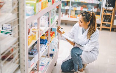 Pharmacist checking Checks Inventory of Medicine, Drugs, Vitamins with tablet and checking patient's prescription in modern pharmacy.