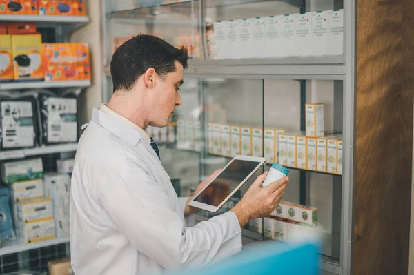 Pharmacist checking Checks Inventory of Medicine, Drugs, Vitamins with tablet and checking patient's prescription in modern pharmacy.