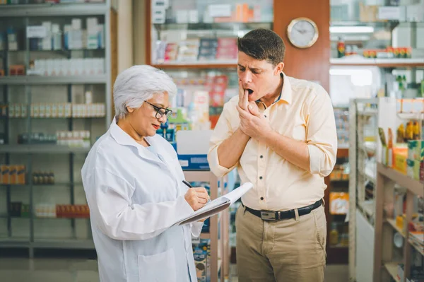 pharmacist is asking about a patient\'s condition in order to prescribe medication according to the patient\'s symptoms who come for prescription consultation in a modern pharmacy.