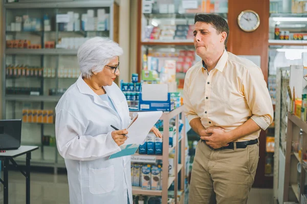 pharmacist is asking about a patient\'s condition in order to prescribe medication according to the patient\'s symptoms who come for prescription consultation in a modern pharmacy.