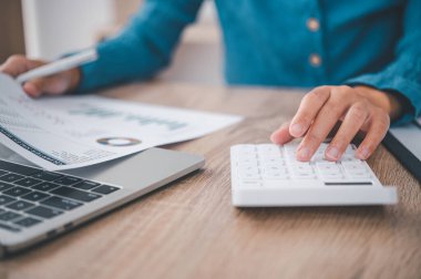 Kapatın. İş adamı hesap makinesinin üzerinde oturuyor ve mali muhasebe konseptinde grafiği var.