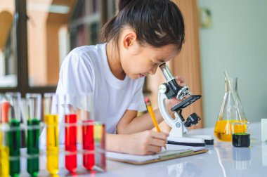 Bilim ve deneyleri öğrenmek için kimyasallarla dolu mikroskop ve test tüplerine bakan küçük bir bilim adamı..