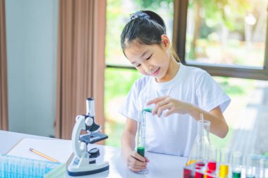 Bilim ve deneyleri öğrenmek için kimyasallarla dolu mikroskop ve test tüplerine bakan küçük bir bilim adamı..