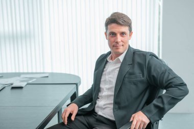 İş kadını, iş arkadaşlarının çalıştığı konferans odasında kameraya bakıyor.