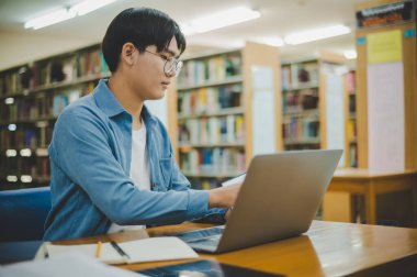 Erkek üniversite öğrencileri dizüstü bilgisayarlar üzerinde çalışıyor ve çalışmak için kitaplar arıyor, raporlar hazırlıyor, üniversite odasında yararlı bilgiler buluyor. Okuma, öğrenme ve zeka kavramı.