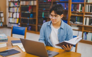 Erkek üniversite öğrencileri dizüstü bilgisayarlar üzerinde çalışıyor ve çalışmak için kitaplar arıyor, raporlar hazırlıyor, üniversite odasında yararlı bilgiler buluyor. Okuma, öğrenme ve zeka kavramı.