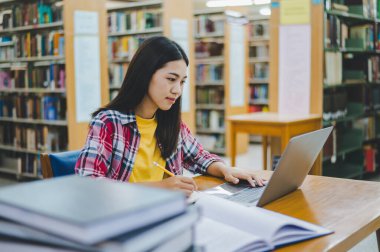 Dizüstü bilgisayarda çalışan ve okuyacak kitaplar arayan, rapor hazırlayan, üniversite odasında işe yarar bilgiler bulan bir üniversite öğrencisi. Okuma, öğrenme ve zeka kavramı.