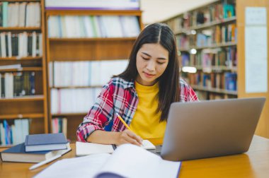 Dizüstü bilgisayarda çalışan ve okuyacak kitaplar arayan, rapor hazırlayan, üniversite odasında işe yarar bilgiler bulan bir üniversite öğrencisi. Okuma, öğrenme ve zeka kavramı.